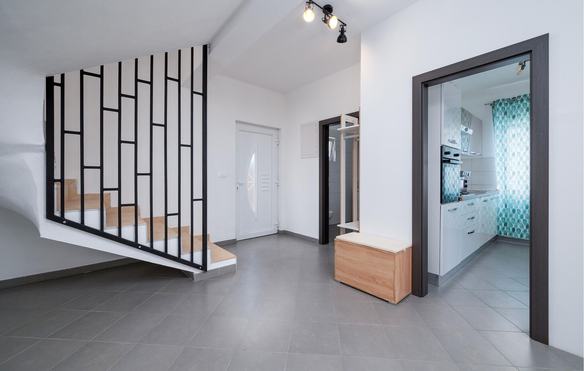 Un interior moderno con una escalera, un banco de madera y una zona de cocina con baldosas estampadas.