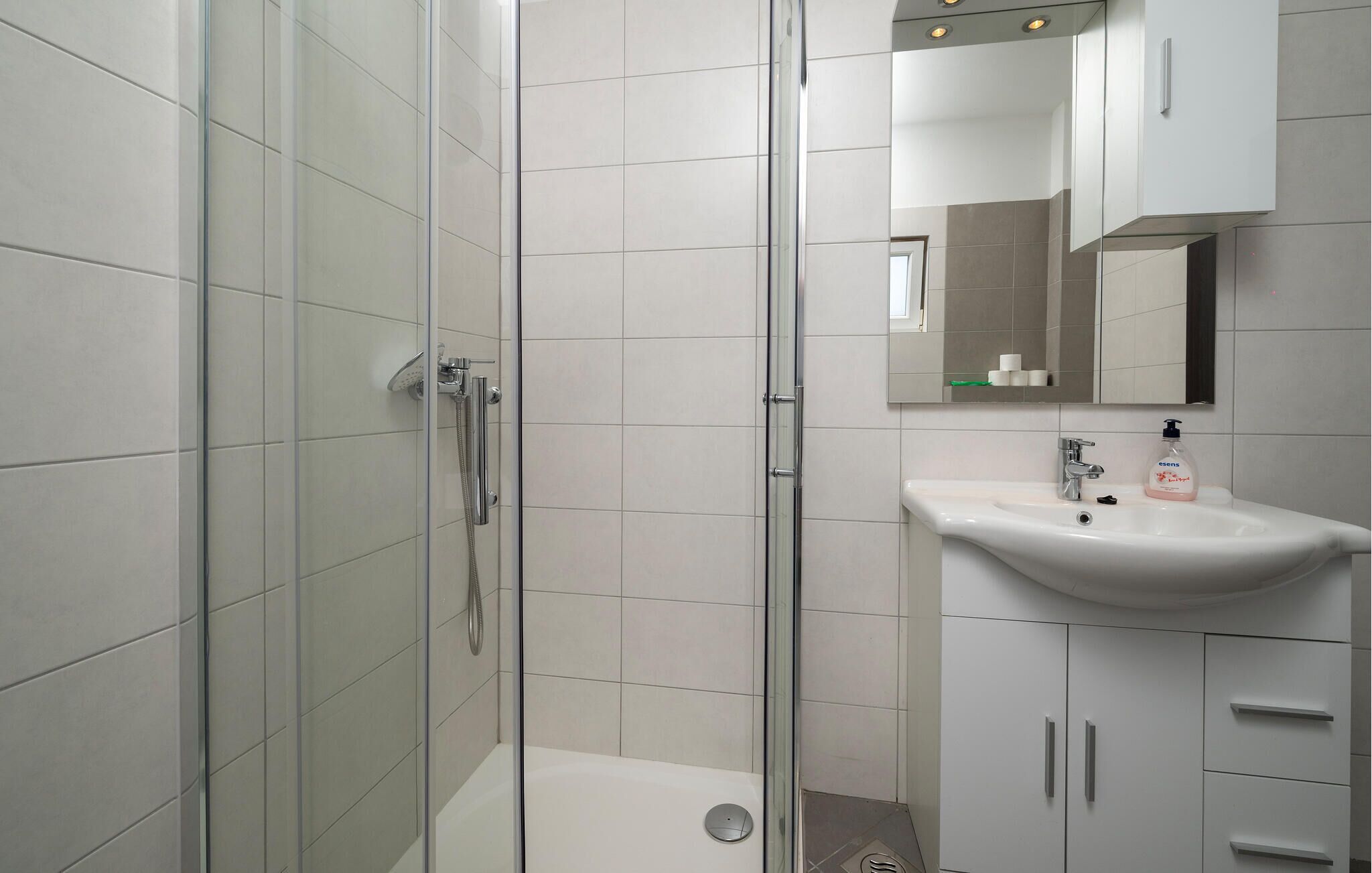 Une salle de bain moderne avec une douche à parois de verre, un lavabo blanc avec un miroir au-dessus et des meubles blancs.