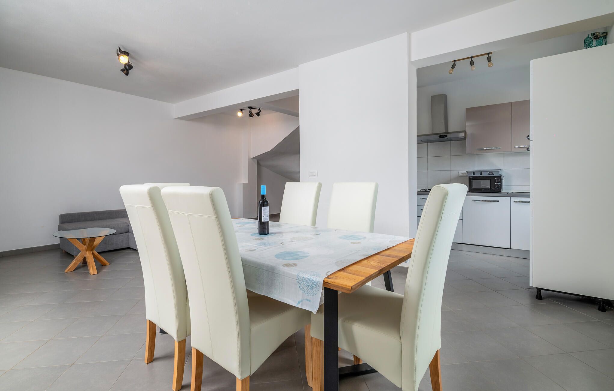 A modern dining area with a table set for four, a sofa, and a kitchen in the background.