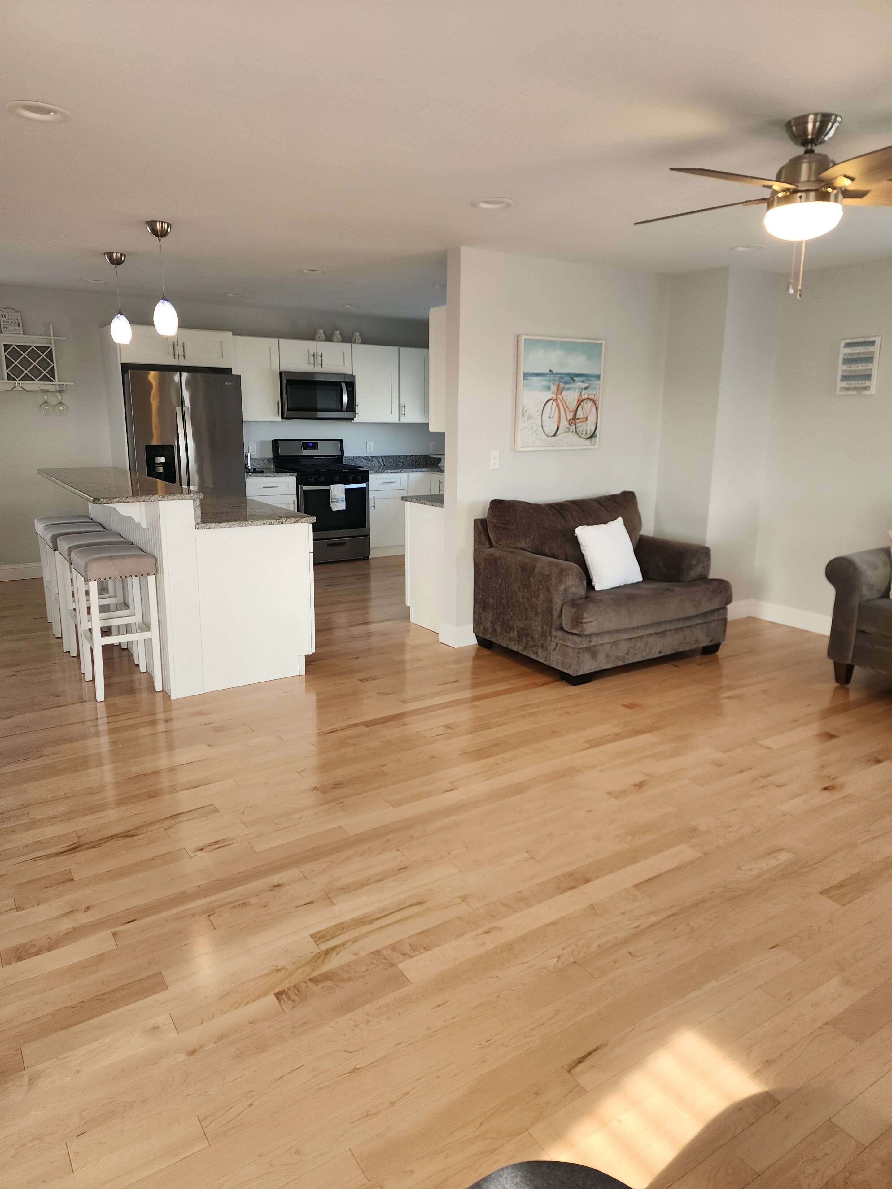 A spacious living area with a kitchen, wooden flooring, a ceiling fan, and a couch.