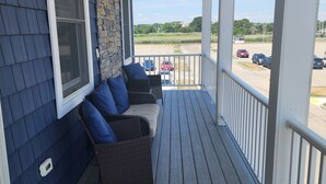 A covered porch with a seating area, a stone wall, and a view of a parking lot. - Spacious Beach Home - Steps to Ocean, Dining & Entertainment (Salisbury)