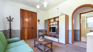 Een woonkamer met een groene bank, houten vloer, een tv-meubel met planken, een houten deur en een kleine tafel met decoratie.