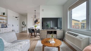 Ett modernt vardagsrum med en soffa, ett soffbord, en tv och en matplats med stolar och ett bord.