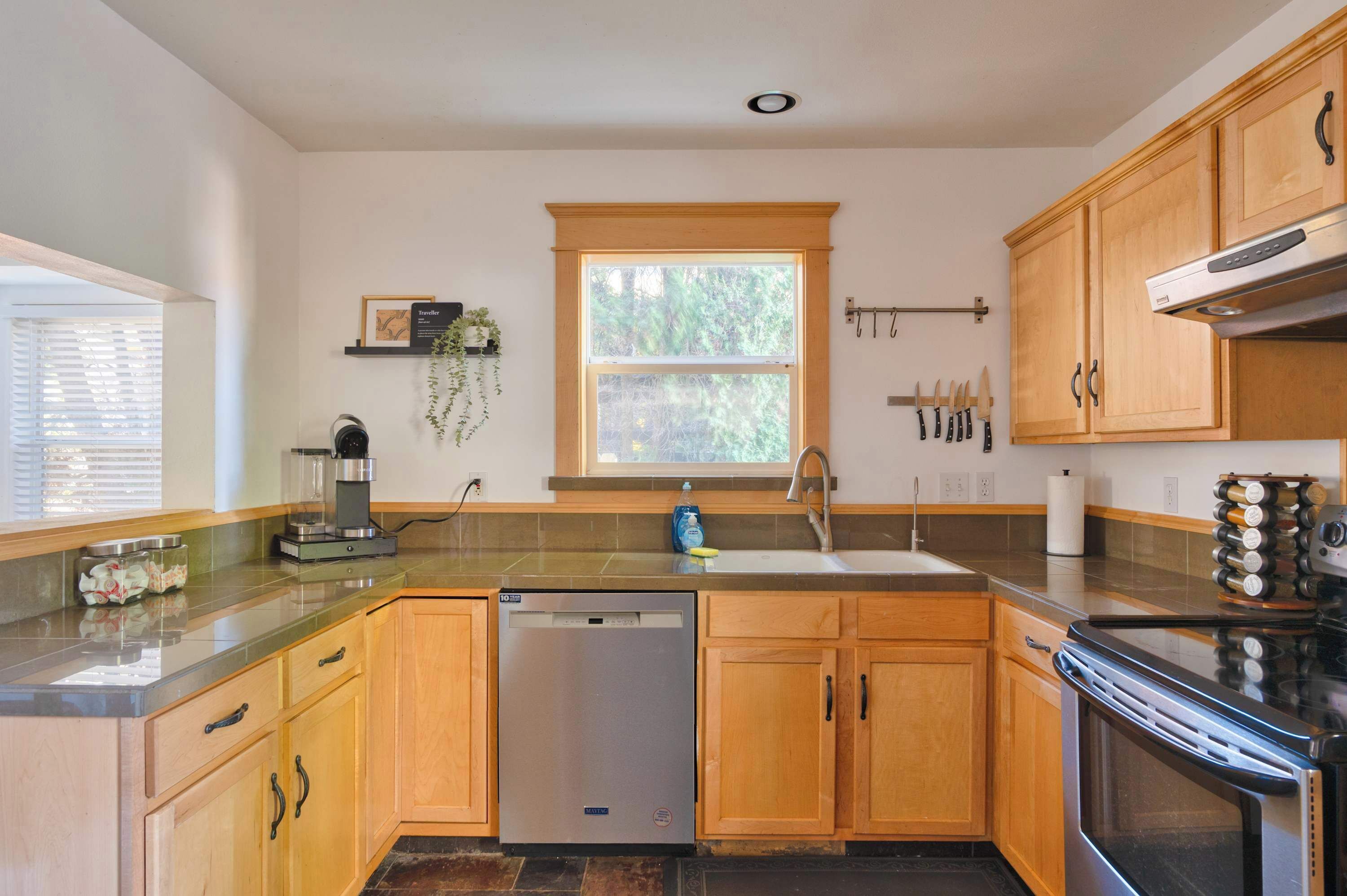 Una cocina con armarios de madera, lavavajillas, estufa y ventana con vista a árboles.