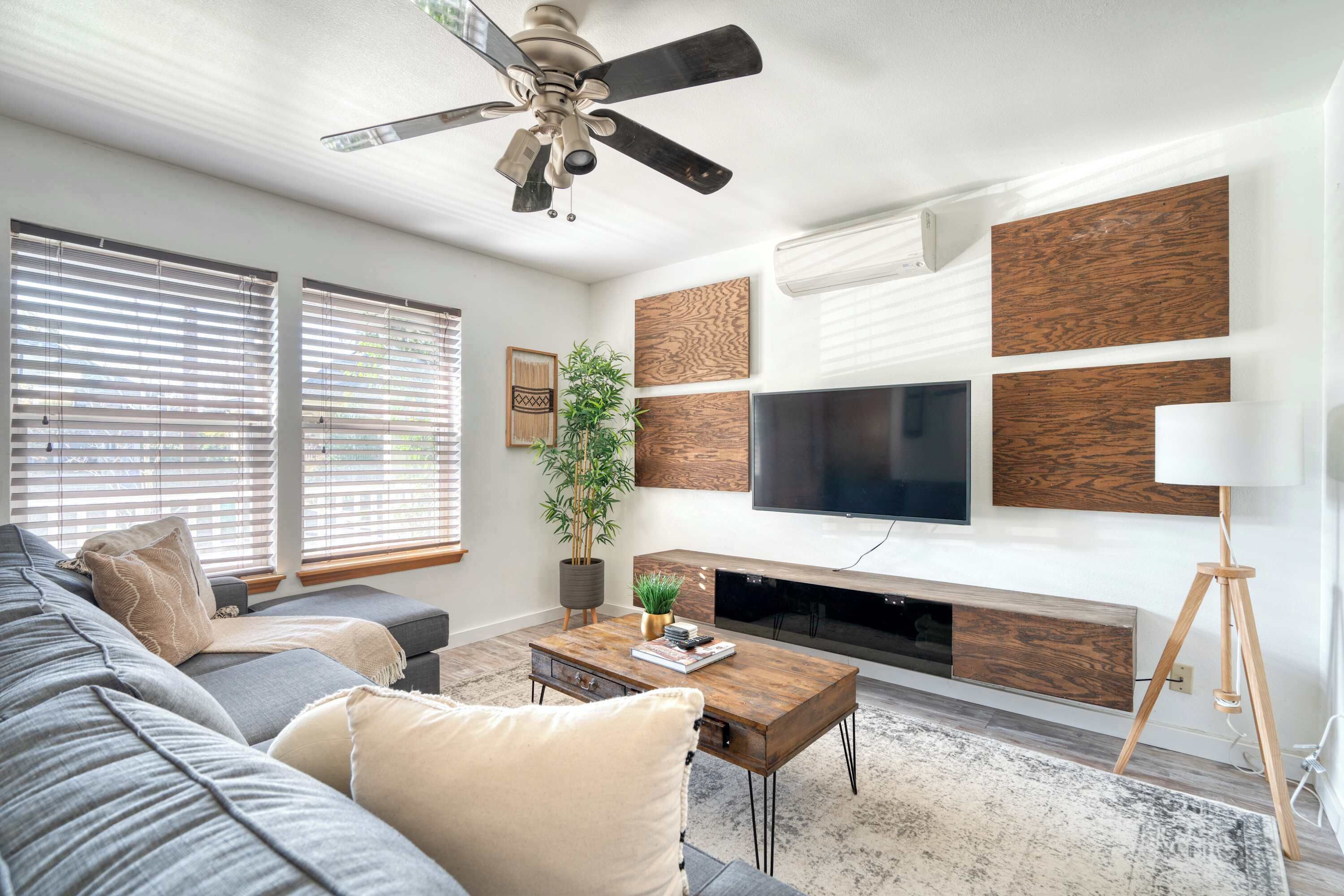 A modern living room with a gray sofa, a wooden coffee table, a TV mounted on the wall, and a ceiling fan.