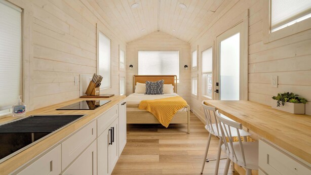 Una stanza compatta e moderna con un letto, una scrivania in legno e angolo cottura.