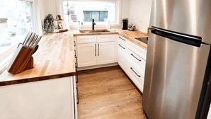 A modern kitchen with white cabinets, a stainless steel refrigerator, and a wooden countertop. - Tiny Retreat • Walk to Bars, Food & Local Art (Portland)