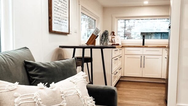 A modern living room with a grey sofa, a framed artwork, and a kitchen visible through an open doorway. - Tiny Retreat • Walk to Bars, Food & Local Art (Portland)