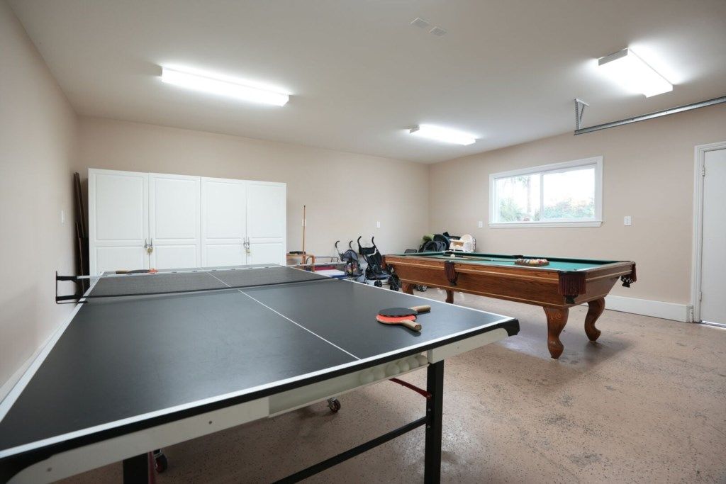 A room with a ping pong table, a pool table, and a white cabinet.
