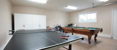 A room with a ping pong table, a pool table, and a white cabinet.