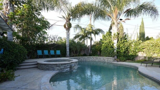 A swimming pool with a stone border, surrounded by palm trees and greenery. - Awesome 4 Bedroom, 3 1/2 Bath Home 1/2 Mile Walk To Disney (Anaheim)