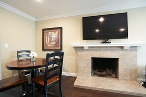 Un comedor con una mesa y sillas, chimenea, televisor montado y un cuadro en la pared.