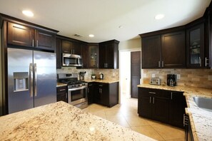 A modern kitchen with dark wood cabinets, stainless steel appliances, granite countertops, and a central island. - Awesome 4 Bedroom, 3 1/2 Bath Home 1/2 Mile Walk To Disney (Anaheim)