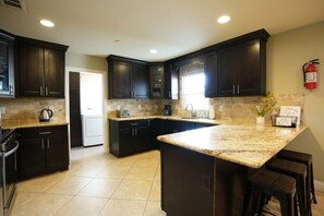 A kitchen with dark cabinets, a granite countertop, and a fire extinguisher on the wall. - Awesome 4 Bedroom, 3 1/2 Bath Home 1/2 Mile Walk To Disney (Anaheim)