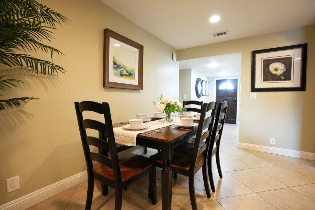 A dining area with a table set for four, chairs, a plant, and framed artwork on the walls.