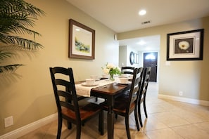 A dining area with a table set for four, chairs, a plant, and framed artwork on the walls.