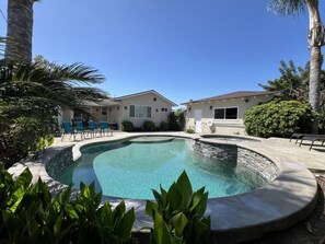 A swimming pool with a curved design, surrounded by a stone deck and palm trees.