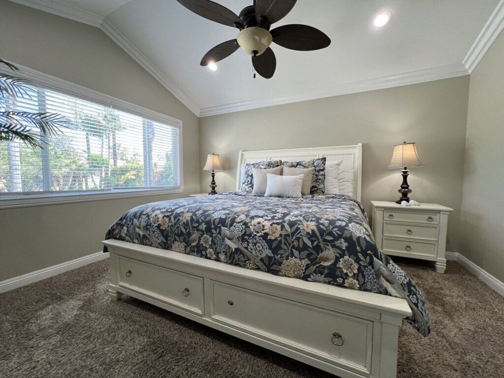 A bedroom with a bed, nightstands, a ceiling fan, and a window with blinds.
