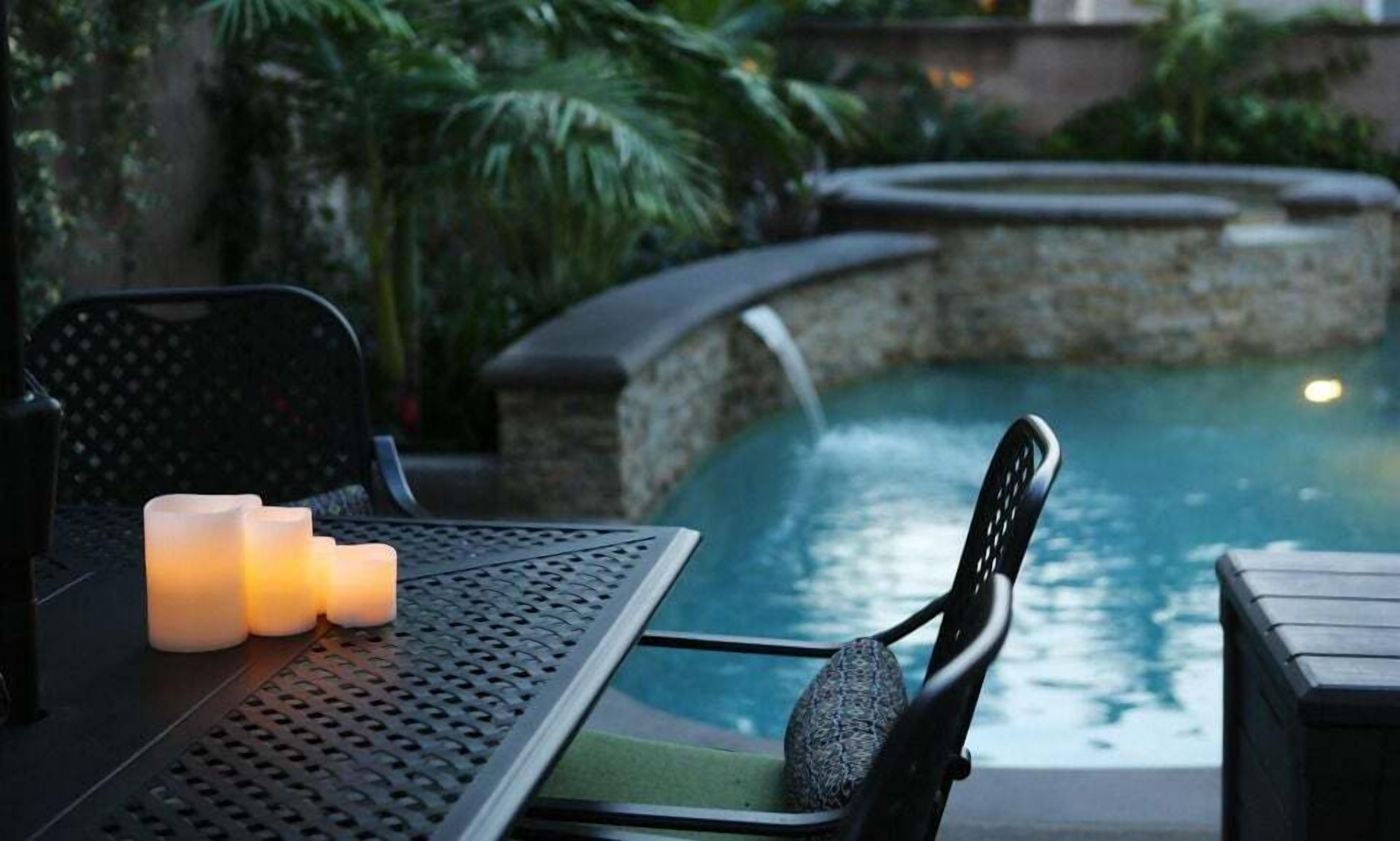 Escena junto a la piscina con una mesa, sillas y velas.
