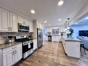 A modern kitchen with white cabinetry, stainless steel appliances, and a wooden floor. - Spectacular 5 Bedroom, 4 Bath Pool Home Near Disney (Anaheim)