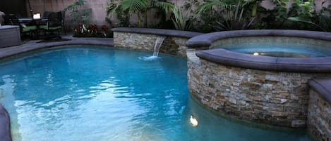 A swimming pool with a waterfall feature and stone walls.