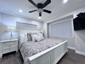 A bedroom with a bed, nightstand, lamp, ceiling fan, and a TV mounted on the wall. - Spectacular 5 Bedroom, 4 Bath Pool Home Near Disney (Anaheim)