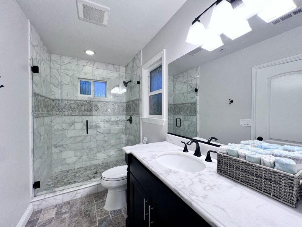 A bathroom with a glass shower enclosure, a white toilet, a marble sink, and a large mirror.