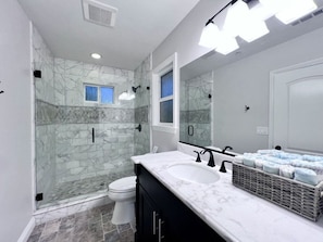 A bathroom with a glass shower enclosure, a white toilet, a marble sink, and a large mirror. - Spectacular 5 Bedroom, 4 Bath Pool Home Near Disney (Anaheim)