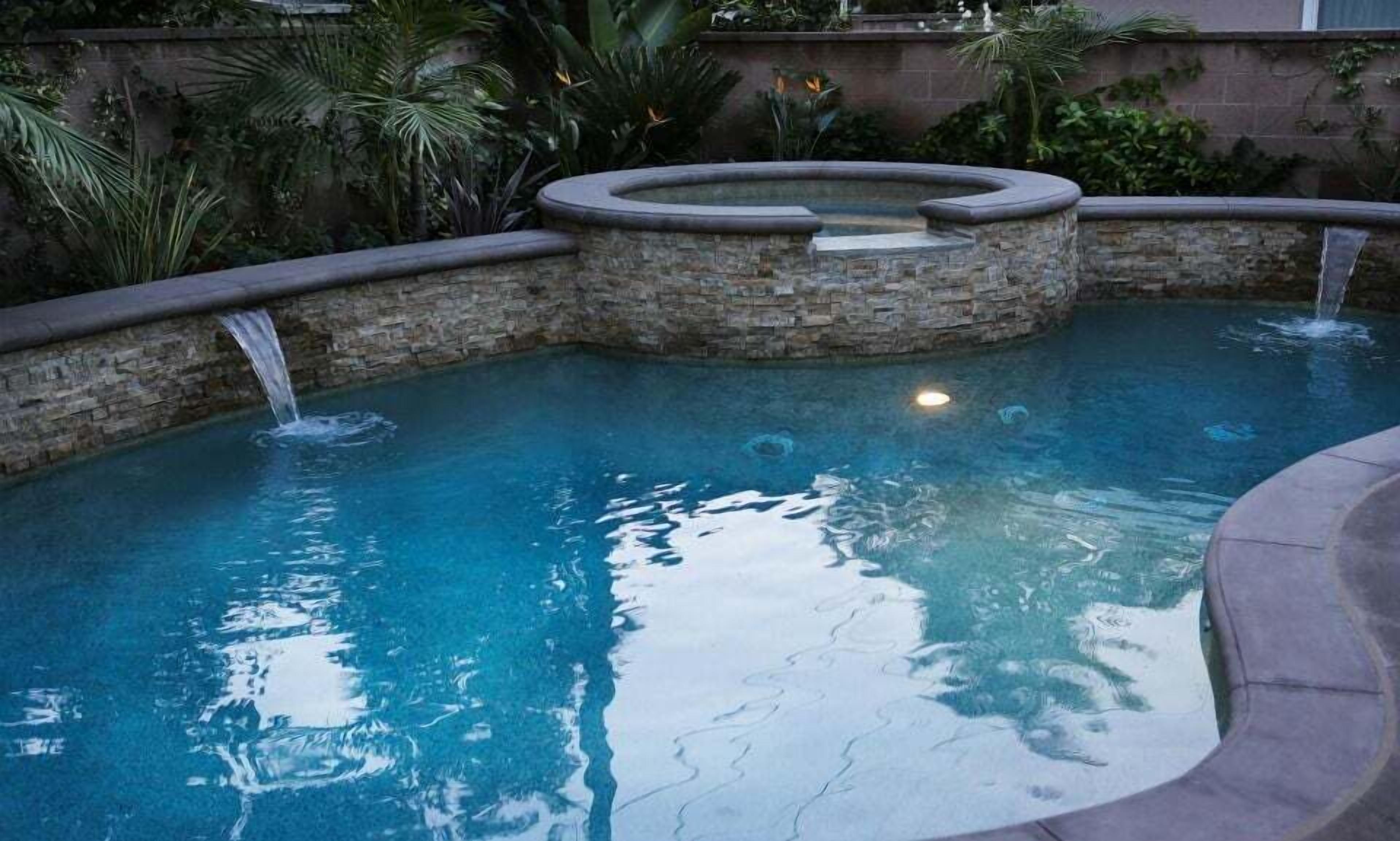 A swimming pool with a stone wall and a hot tub.