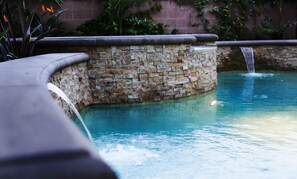 A stone pool with a waterfall feature, surrounded by a stone wall and greenery. - Destination #28 (Anaheim)