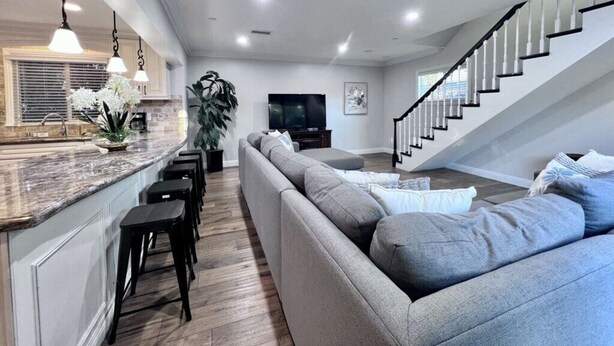 A modern living room with a grey sofa, black bar stools, a kitchen island, and a staircase. - Spectacular 5 Bedroom, 4 Bath Pool Home Near Disney (Anaheim)