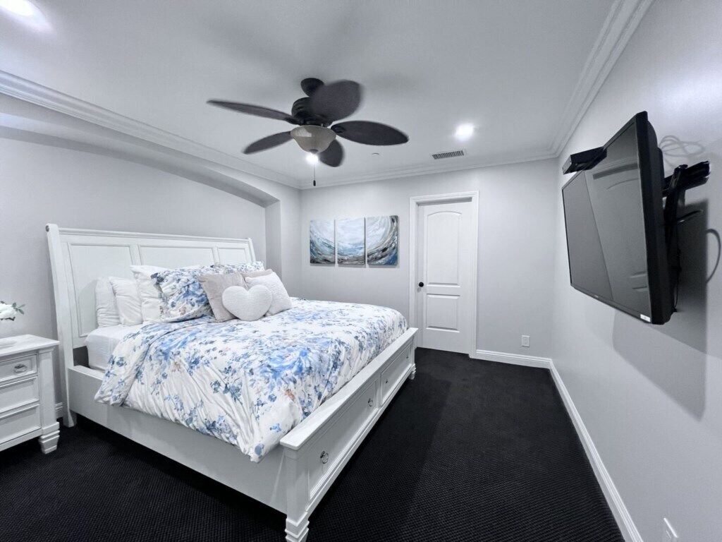 Een slaapkamer met een bed, een plafondventilator, een televisie en een deur.