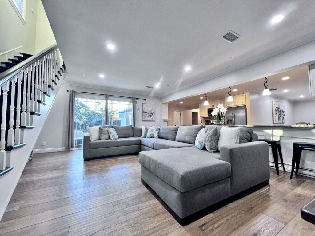 Una sala moderna con un sofá modular, una escalera y una zona de cocina.