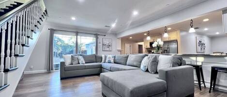 Una sala moderna con un sofá modular, una escalera y una zona de cocina.