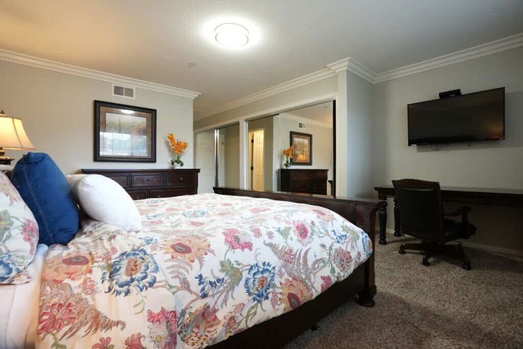 Une chambre d’hôtel avec un grand lit, un bureau, une chaise, un téléviseur à écran plat et un miroir.