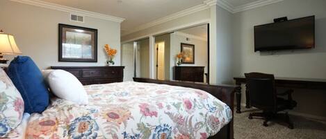 A hotel room with a large bed, a desk, a chair, a flat-screen TV, and a mirror.