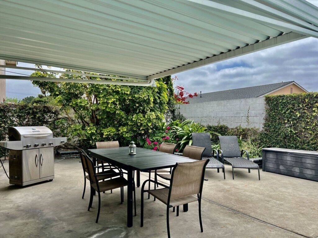 Un patio exterior con una parrilla, una mesa de comedor y sillas.