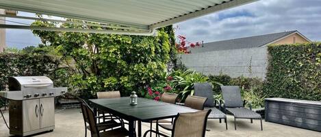 An outdoor patio with a grill, dining table, and chairs.