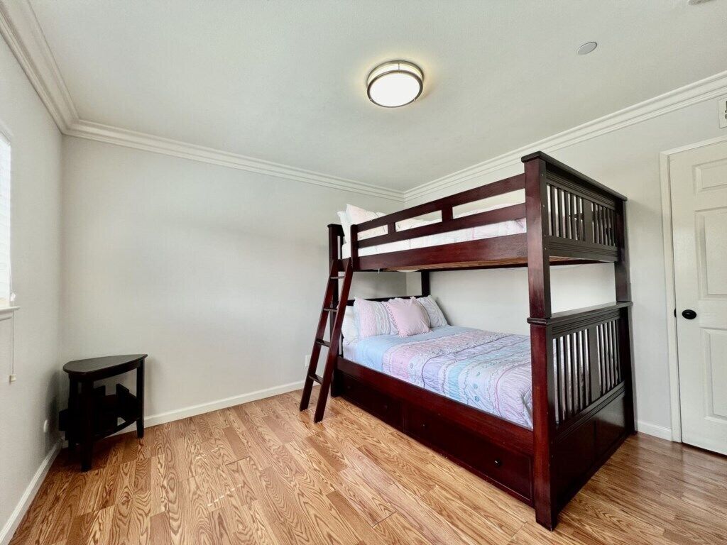 A bunk bed in a room with wooden flooring, a small table, and a door.