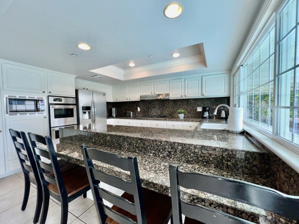 A kitchen with white cabinets, granite countertops, and a large island with chairs.