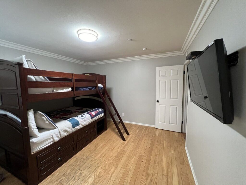 A bedroom with a bunk bed, a dresser, a door, and a TV mounted on the wall.