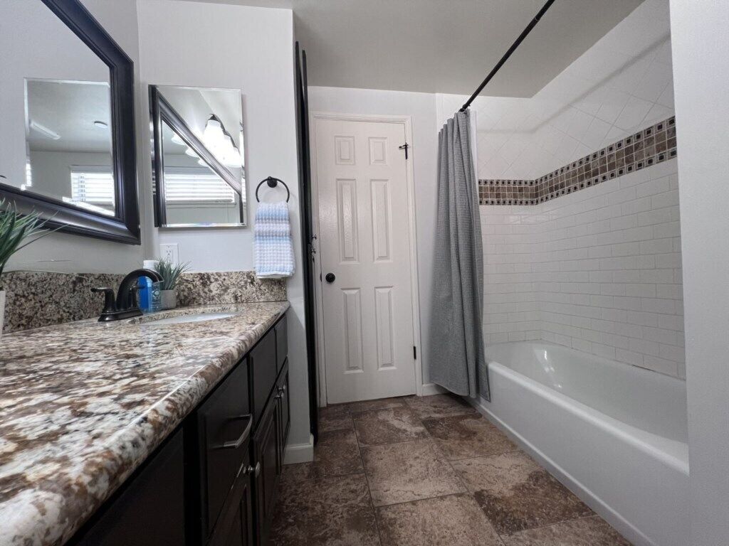 Un bagno con una porta bianca, una tenda da doccia, una vasca e un lavabo su un piano in granito.