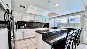 A modern kitchen with white cabinets, a granite countertop, and a large island with bar stools. - Large Family Pool Home 2.5 Miles To Disney w/3 King Beds!!! (Anaheim)