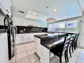 A modern kitchen with white cabinets, a granite countertop, and a large island with bar stools.
