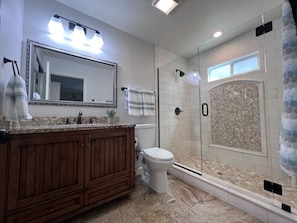 A bathroom with a vanity, toilet, shower, and a large mirror.