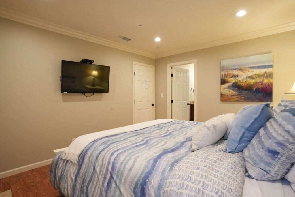 A bedroom with a bed, a TV mounted on the wall, a door, and a painting.