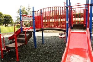 A playground with red and blue equipment, including slides and climbing structures.