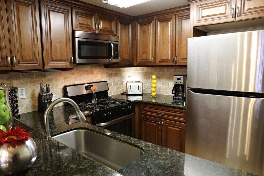Una cocina con armarios de madera, un refrigerador de acero inoxidable, un microondas, una estufa y un lavamanos.