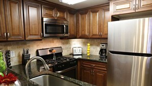 Una cocina con armarios de madera, un refrigerador de acero inoxidable, un microondas, una estufa y un lavamanos.