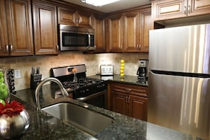 A kitchen with wooden cabinets, a stainless steel refrigerator, a microwave, a stove, and a sink.